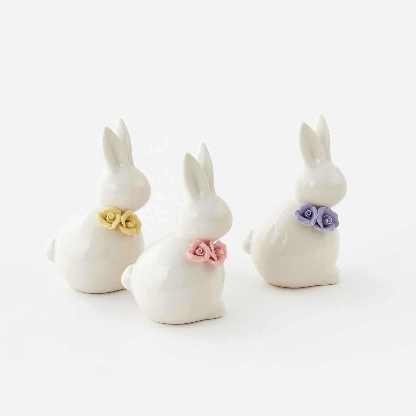 Three white ceramic bunny figurines with colorful flower collars on a white background