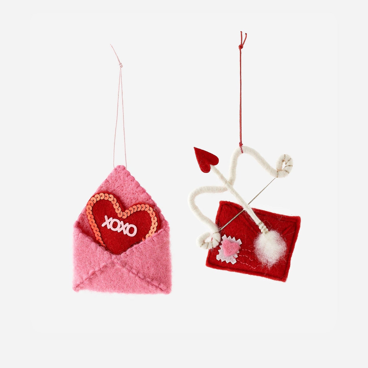 Two felt decorations on a white background, one pink envelope with a heart and 'XOXO' text, the other red square with a white pom-pom.