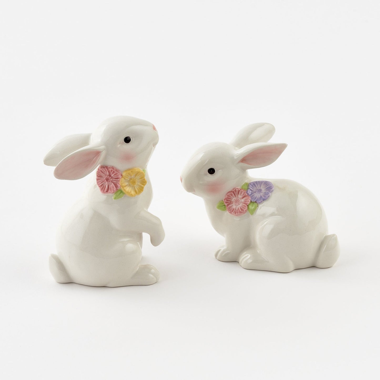 Two white ceramic rabbits with floral bows on a white background