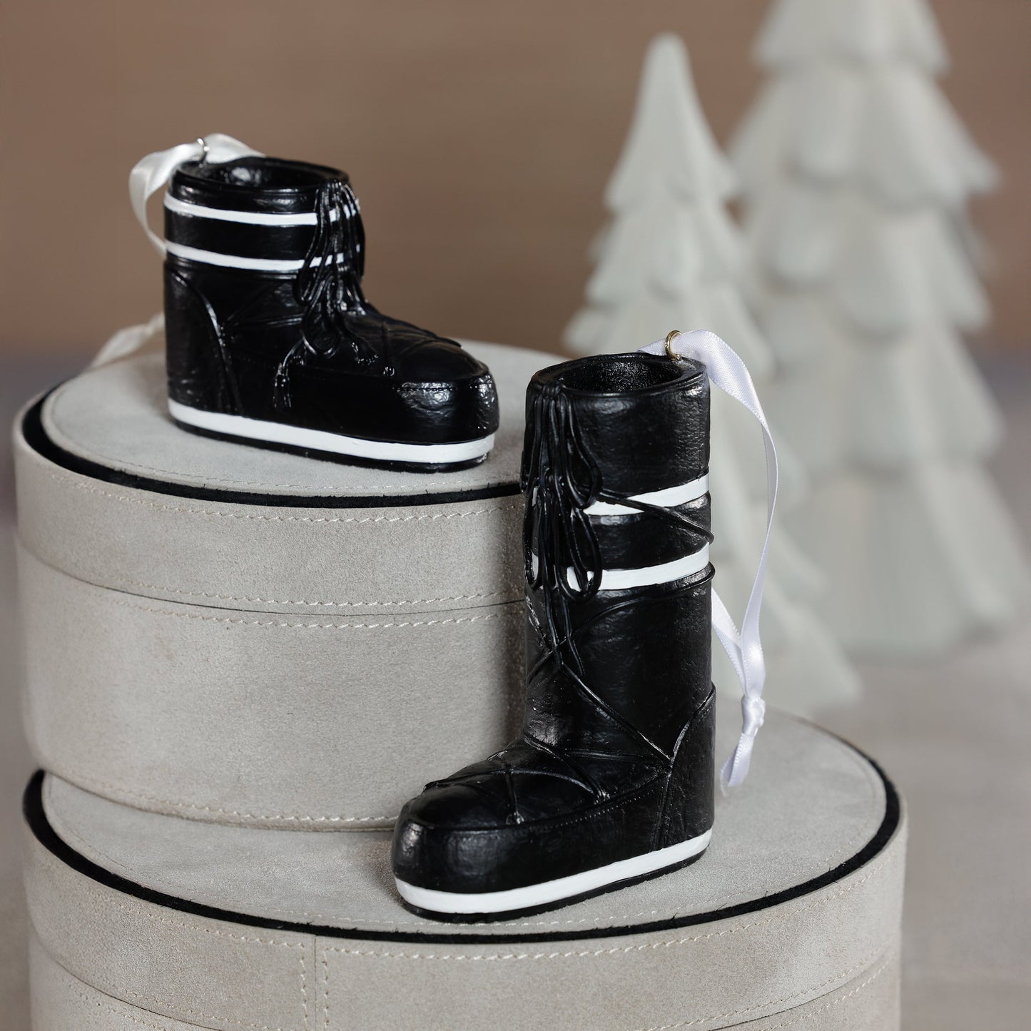 Black boots with white stripes on a beige cylindrical stand against a neutral background
