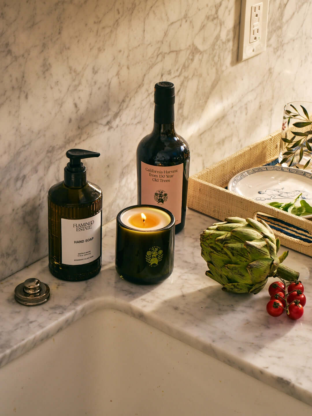 Flamingo Estate hand soap and candle displayed on marble countertop with fresh vegetables.