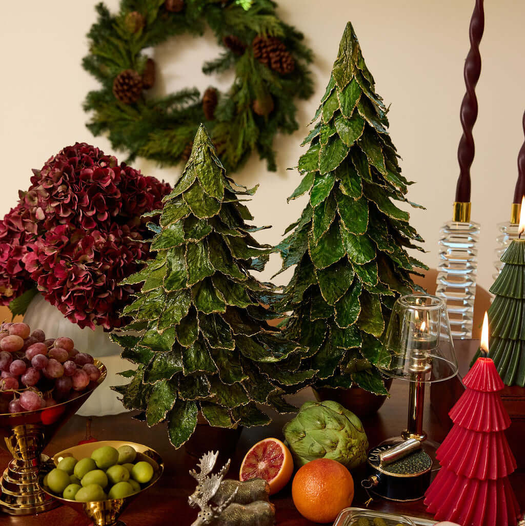 Decorative Christmas Trees surrounded by festive fruits and holiday decor on a wooden table.