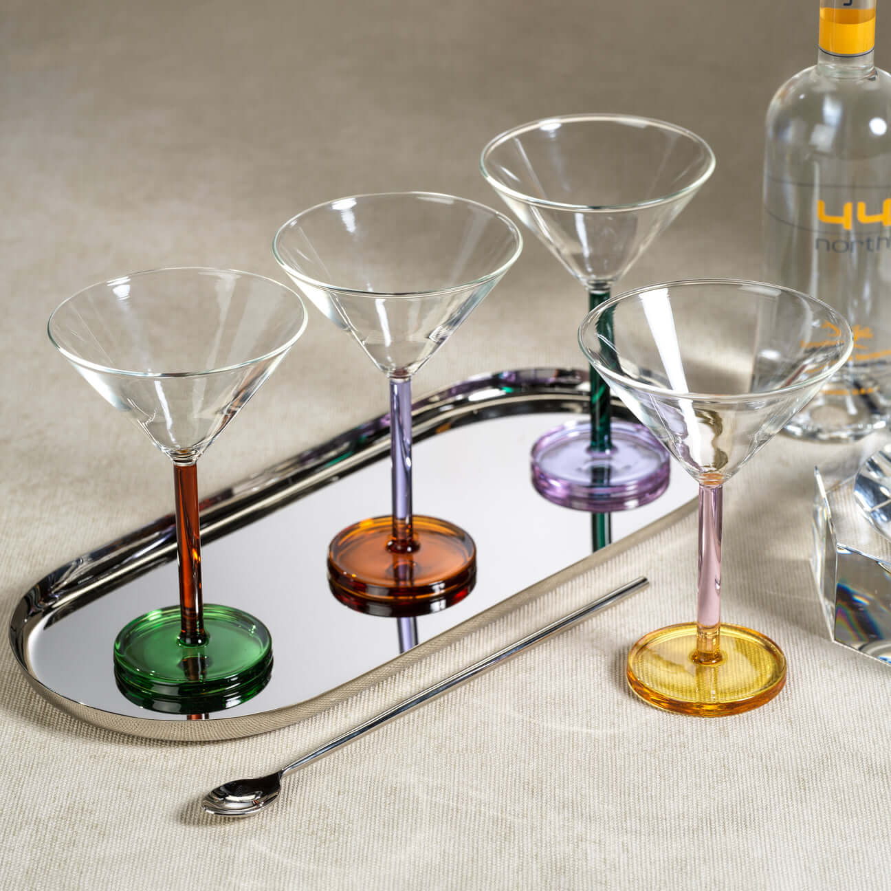 Colorful Martini Glasses displayed on a reflective tray with a cocktail shaker and a spoon.