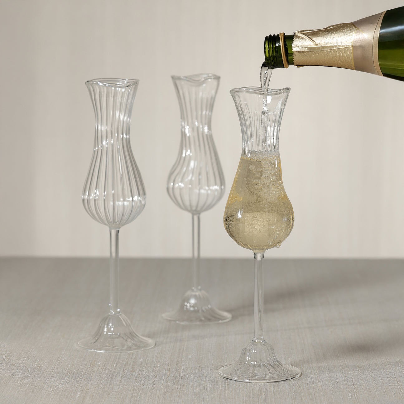 Pouring champagne into a elegant Champagne Glasses with three decoraive glass pieces in the background.