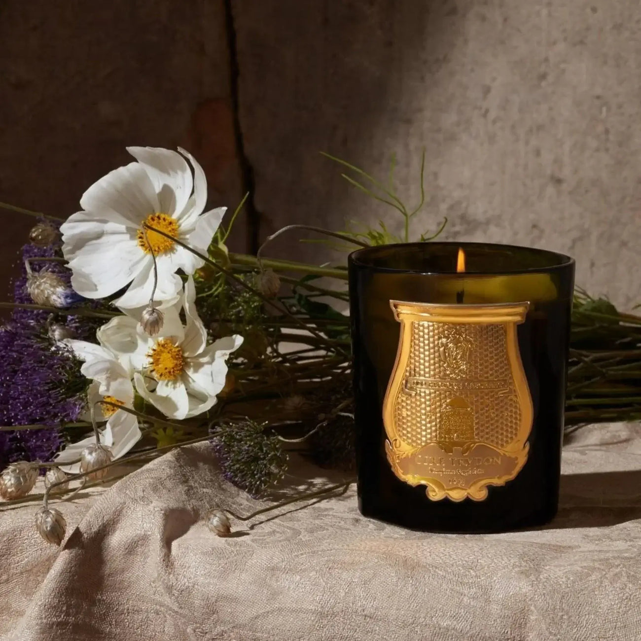 Trudon candle displayed with flowers on a textured surface, showcasing its elegant design and warm glow.
