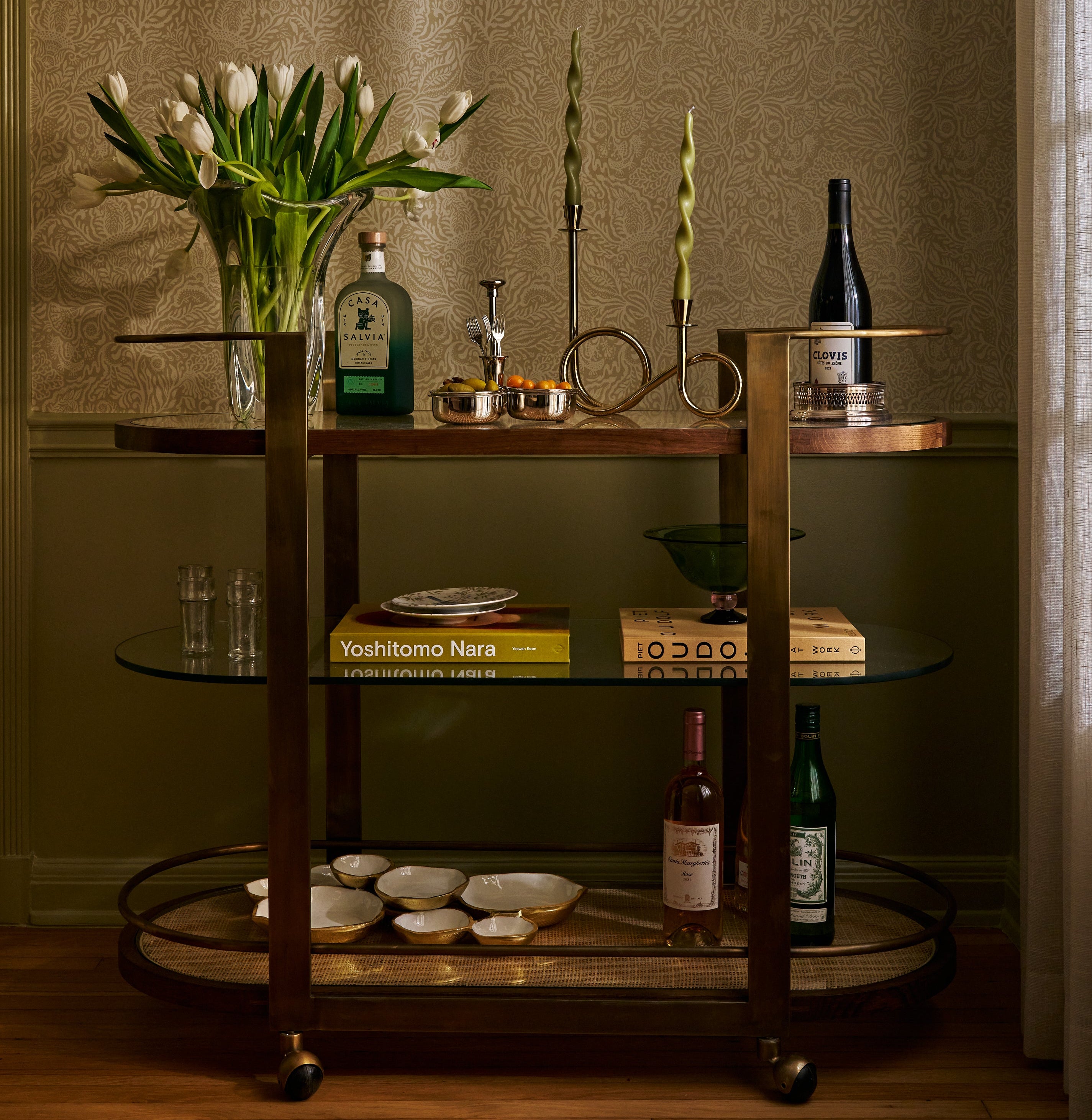 Decorative setup with candles, bottles, and flowers against a patterned wall.