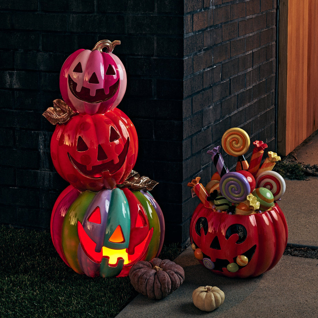 A set of Halloween decorative jack-o'-lantern pumpkins and candy-filled gourds arranged outdoors on a patio and brick wall, with warm lights glowing inside the pumpkins.