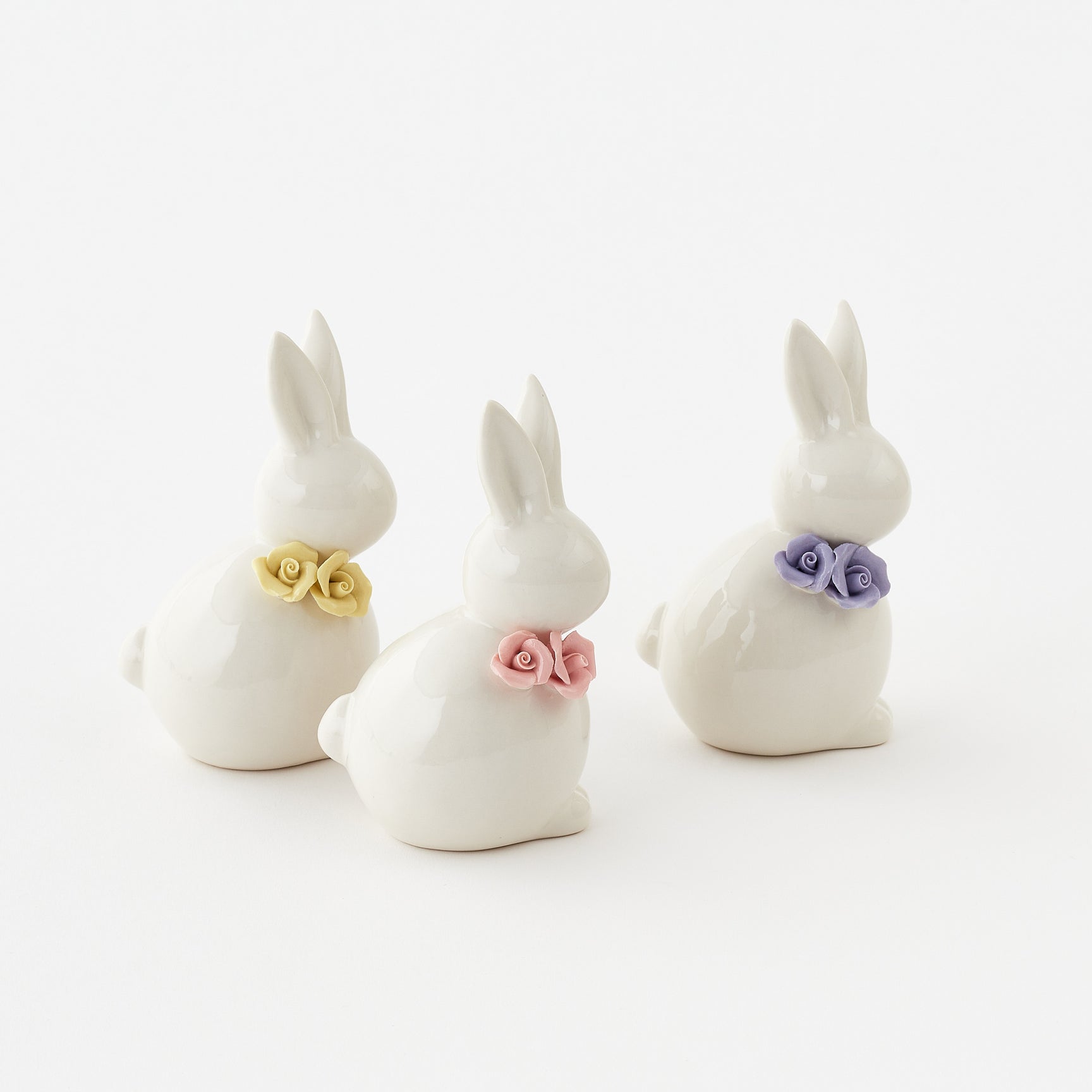 Three white ceramic bunny figurines with colorful flower collars on a white background