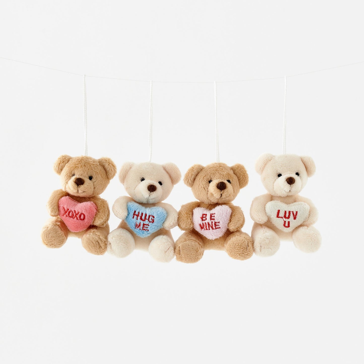 Four teddy bears with heart-shaped messages hanging against a white background
