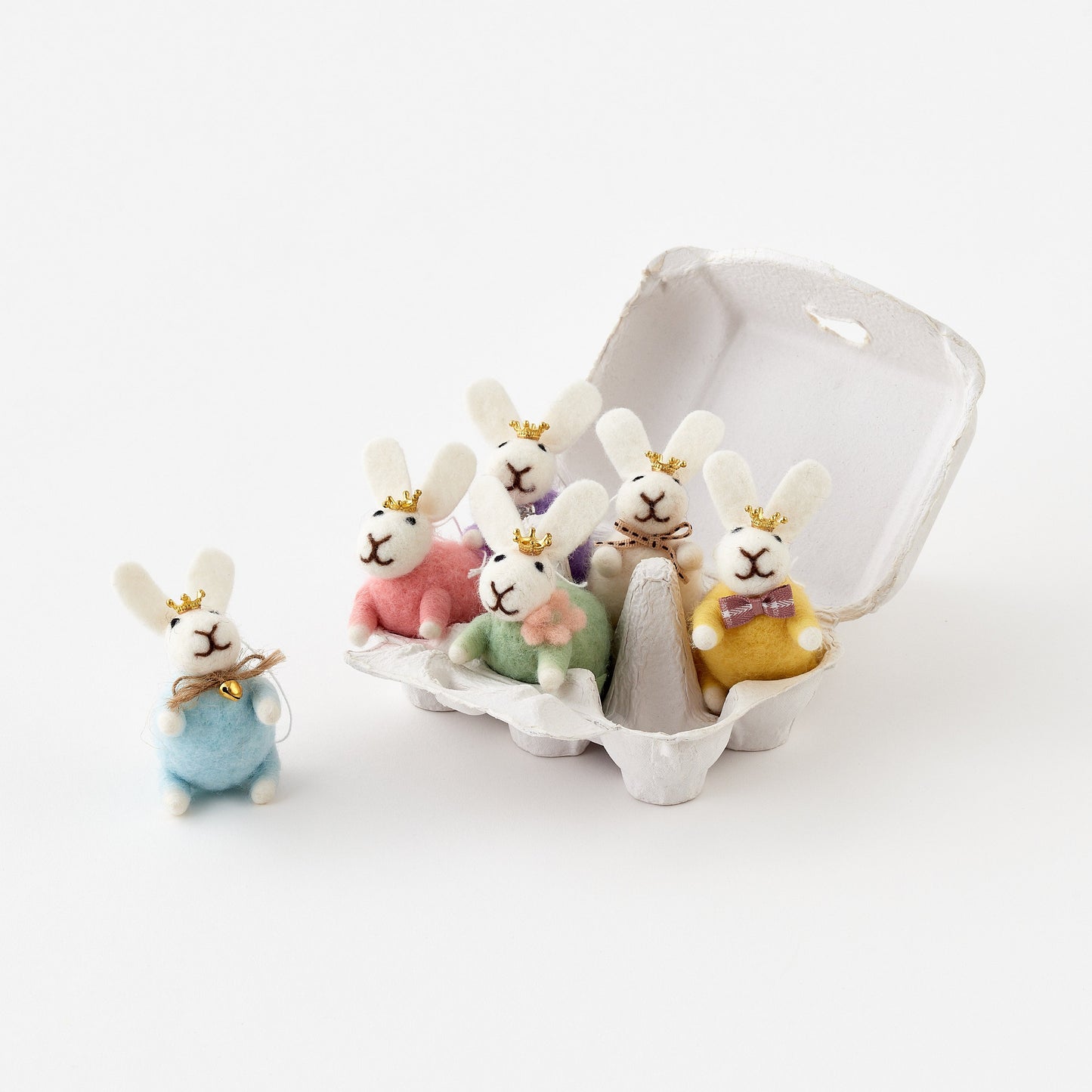 Set of small rabbit figurines in a white egg carton on a light background