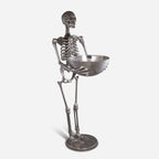 Metallic skeleton figurine holding a bowl on a white background