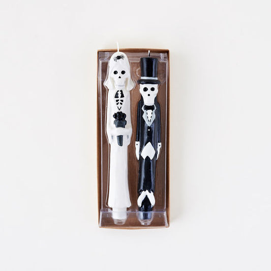 Two skeleton candles, one in a top hat and bow tie, the other in a suit, in packaging on a white background.