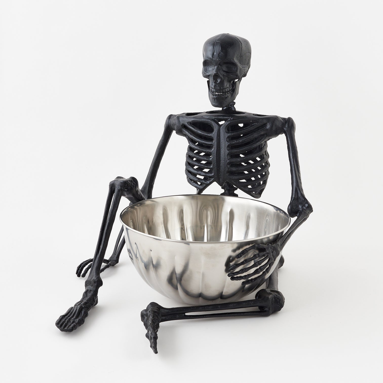 Black skeleton figurine holding a silver bowl on a white background