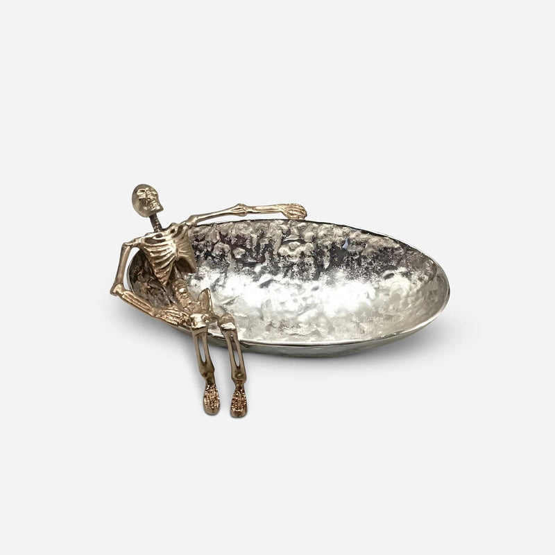 A silver-toned metal figurine of a seated figure holding a hammered oval tray, photographed on a clean light gray background.