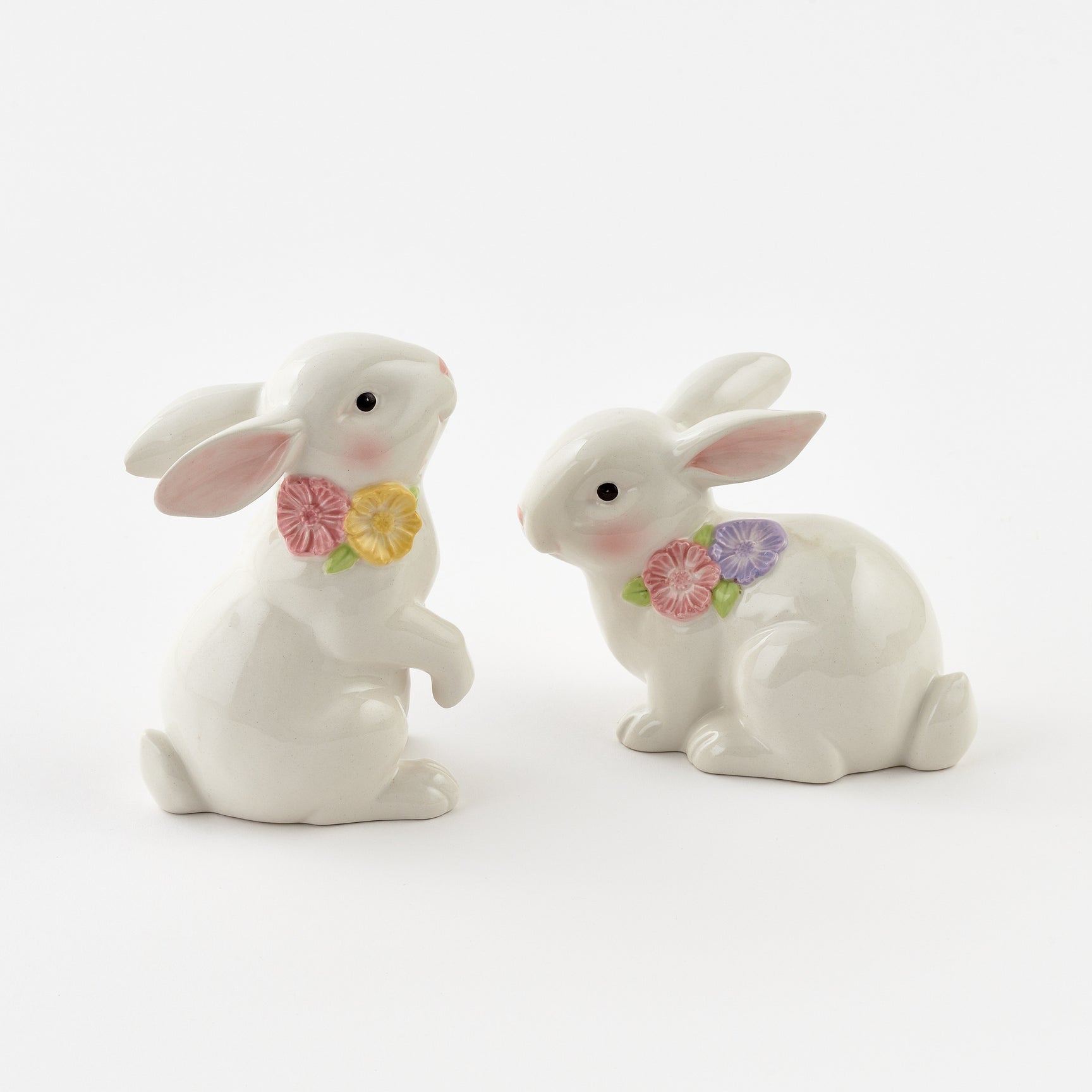 Two white ceramic rabbits with floral bows on a white background