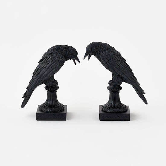 Two black crow statues on stands against a white background