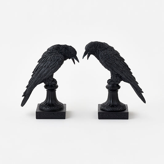 Two black crow statues on stands against a white background