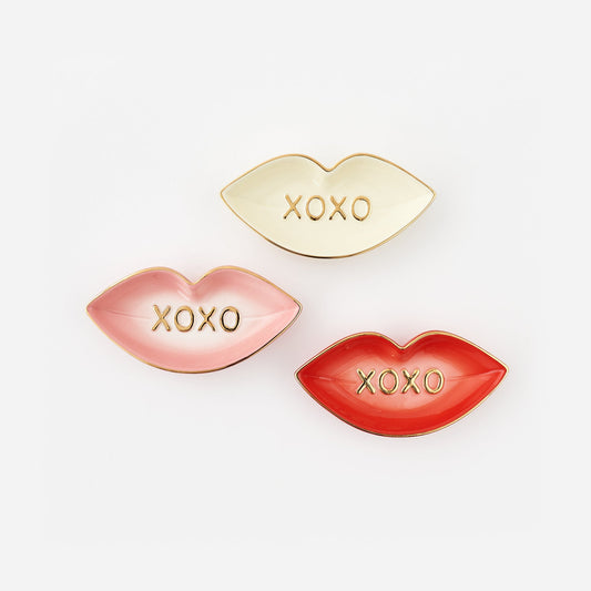 Three lip-shaped trinket dishes in gold, pink, and red with 'XOXO' text on a white background.