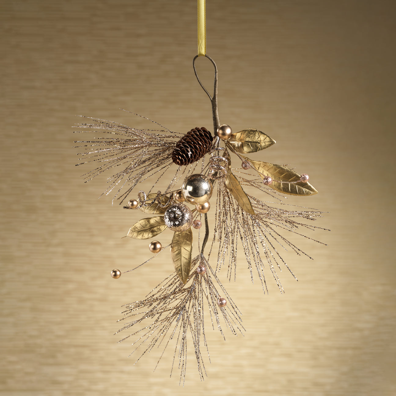 Decorative ornament with gold leaves, pinecones, and beads on a beige background