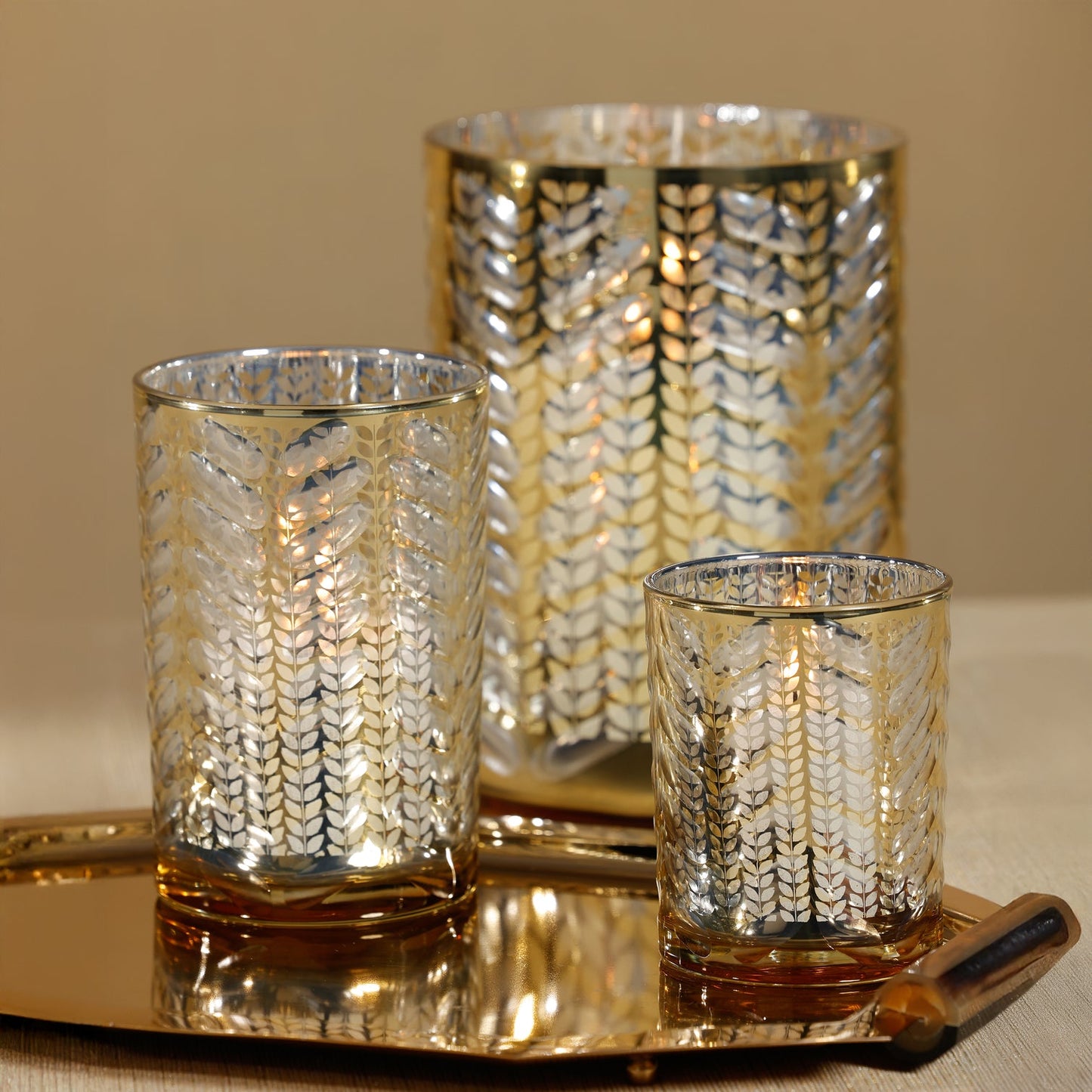 Set of three gold and silver patterned candle holders on a tray with a neutral background.