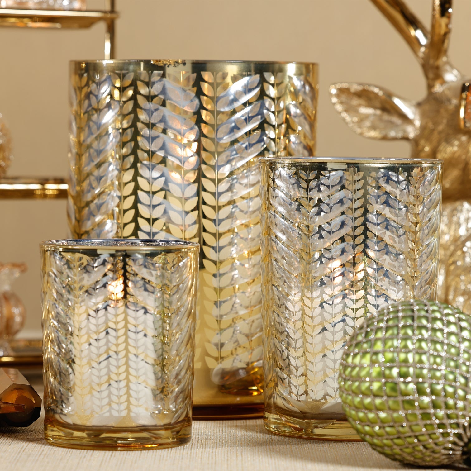 Decorative glass hurricanes with gold and silver patterns on a neutral background
