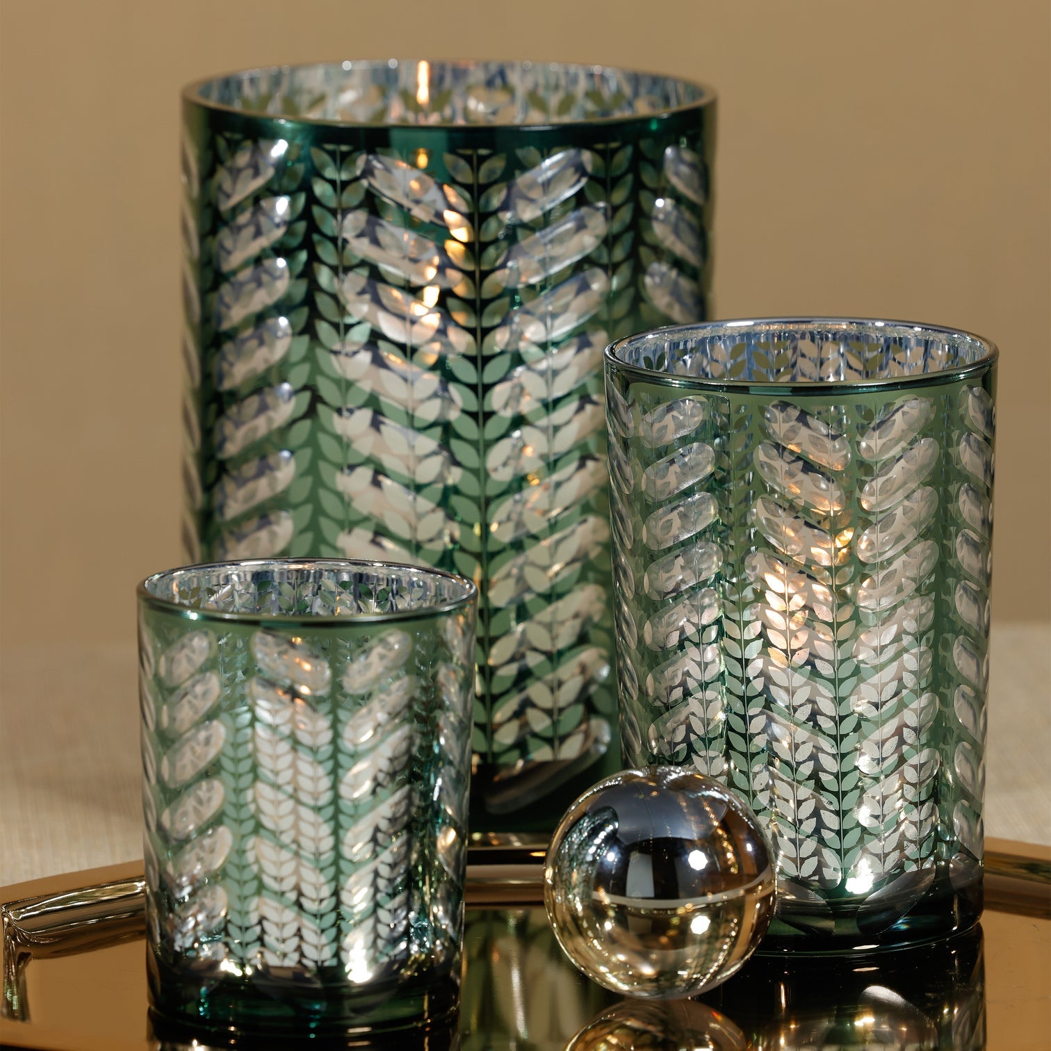 Set of three decorative glass vases with leaf pattern on a reflective surface.