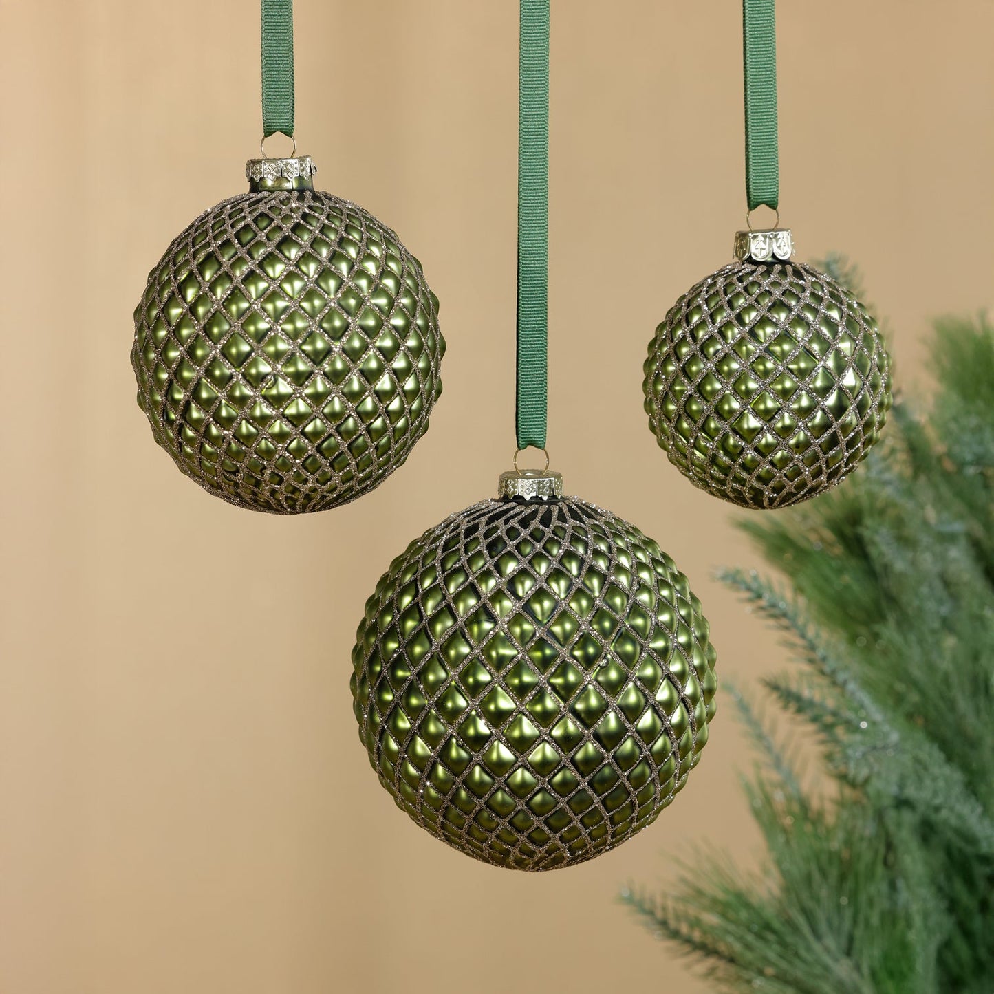 Three green textured Christmas ornaments on a beige background with a tree branch.