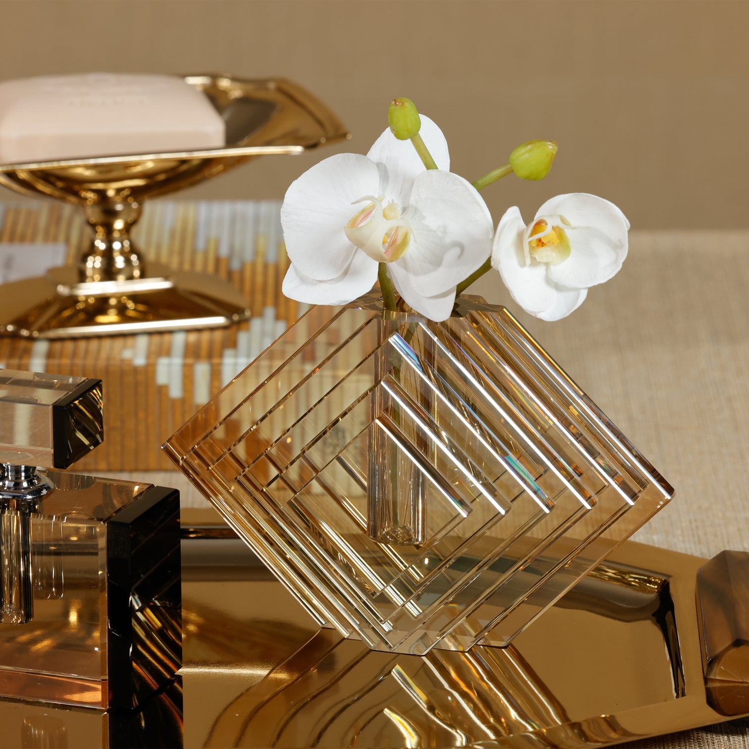Decorative glass vase with white orchids on a reflective surface with gold and beige background