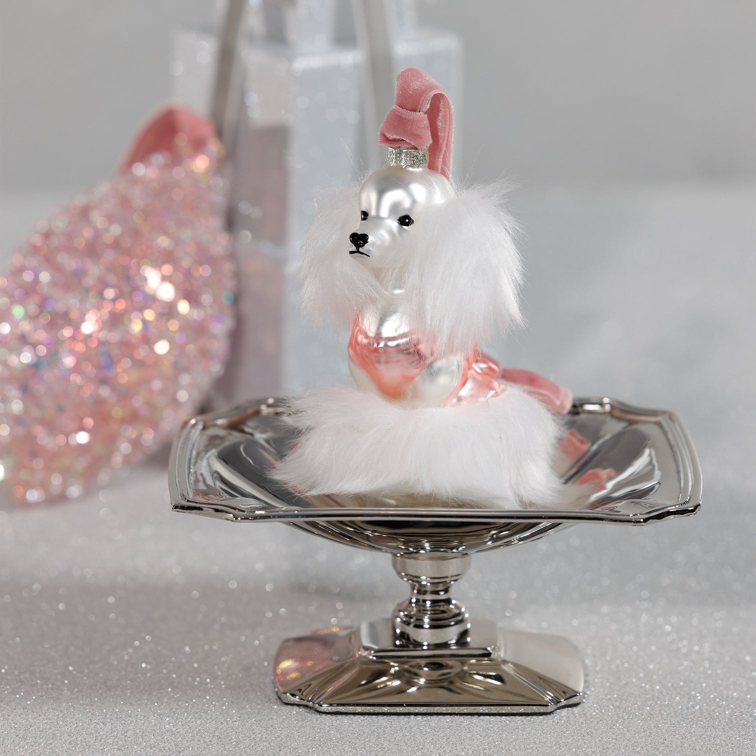 Decorative dog figurine on a silver stand with a pink hat against a glittery background