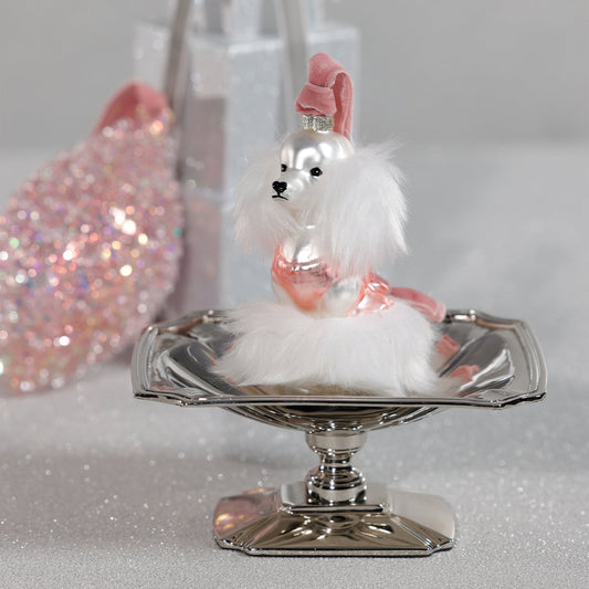 Decorative dog figurine on a silver stand with a pink hat against a glittery background