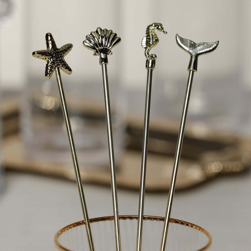 Four decorative stir sticks with starfish, shell, seahorse, and whale tail ends on a stand.