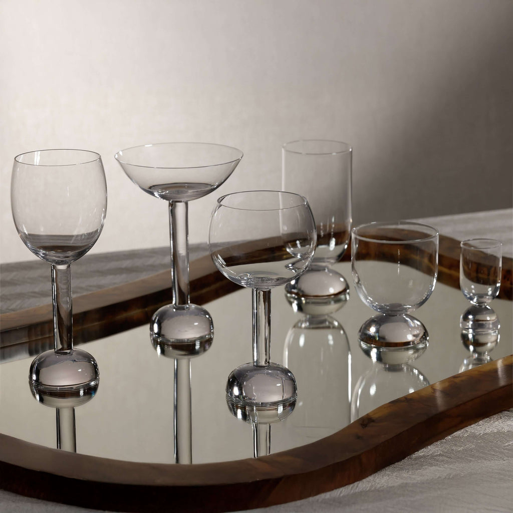 Elegant Madrid Glassware Collection displayed on a mirror tray, featuring sculptural glass designs with solid sphere bases.