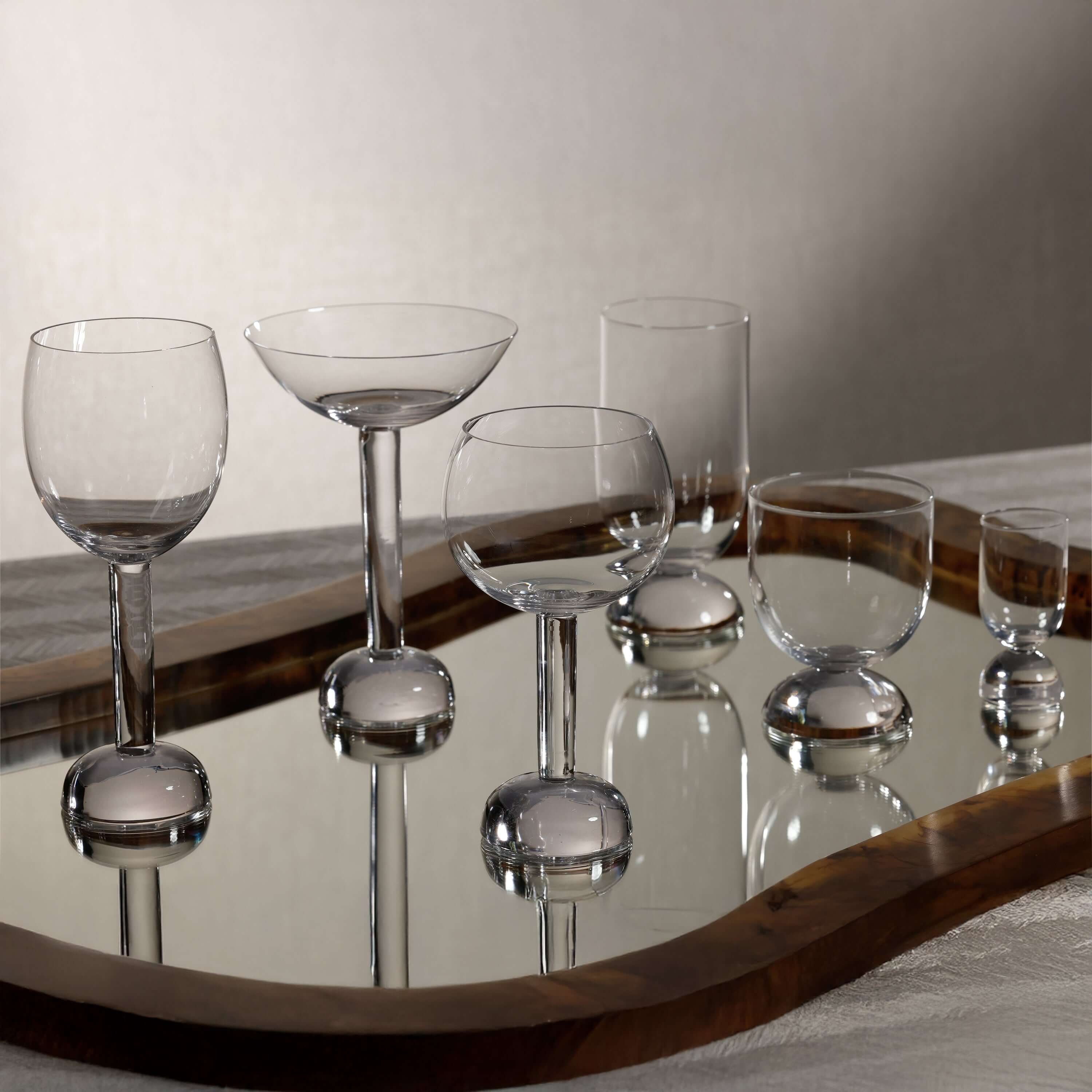 Elegant Madrid Glassware Collection displayed on a mirror tray, featuring sculptural glass designs with solid sphere bases.