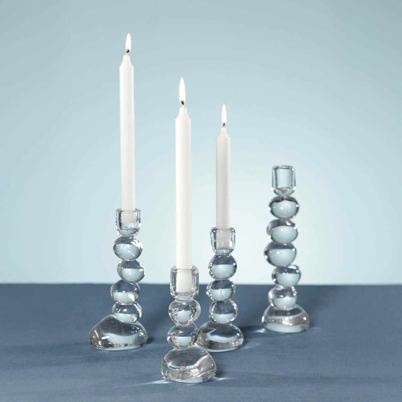 Ice Stone Glass Taper Holder displayed with glowing candles on a blue table.