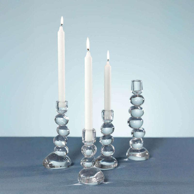 Ice Stone Glass Taper Holder displayed with glowing candles on a blue table.