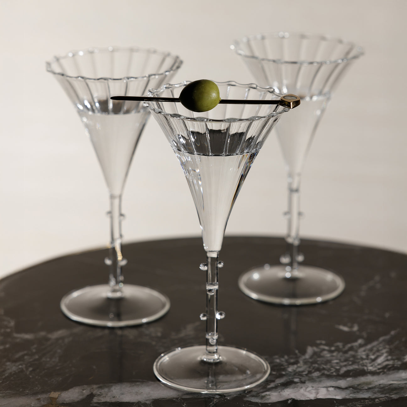Three martini glasses on a dark surface with a white background