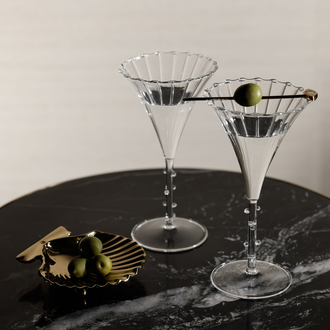 Two martini glasses with olive garnishes on a dark surface.