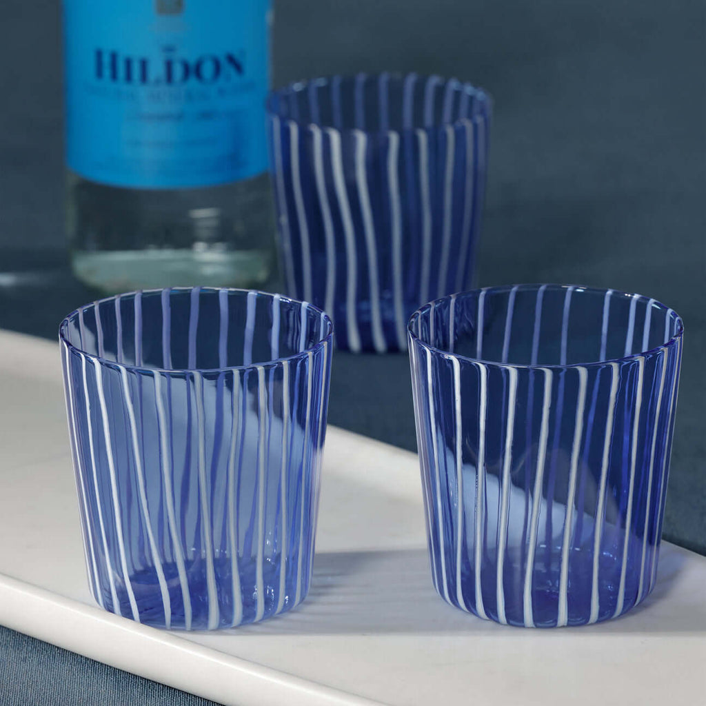 Marina White Stripe Glass Tumbler (Set of 6) in blue with white vertical stripes on a marble tray.