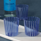 Marina White Stripe Glass Tumbler (Set of 6) in blue with white vertical stripes on a marble tray.