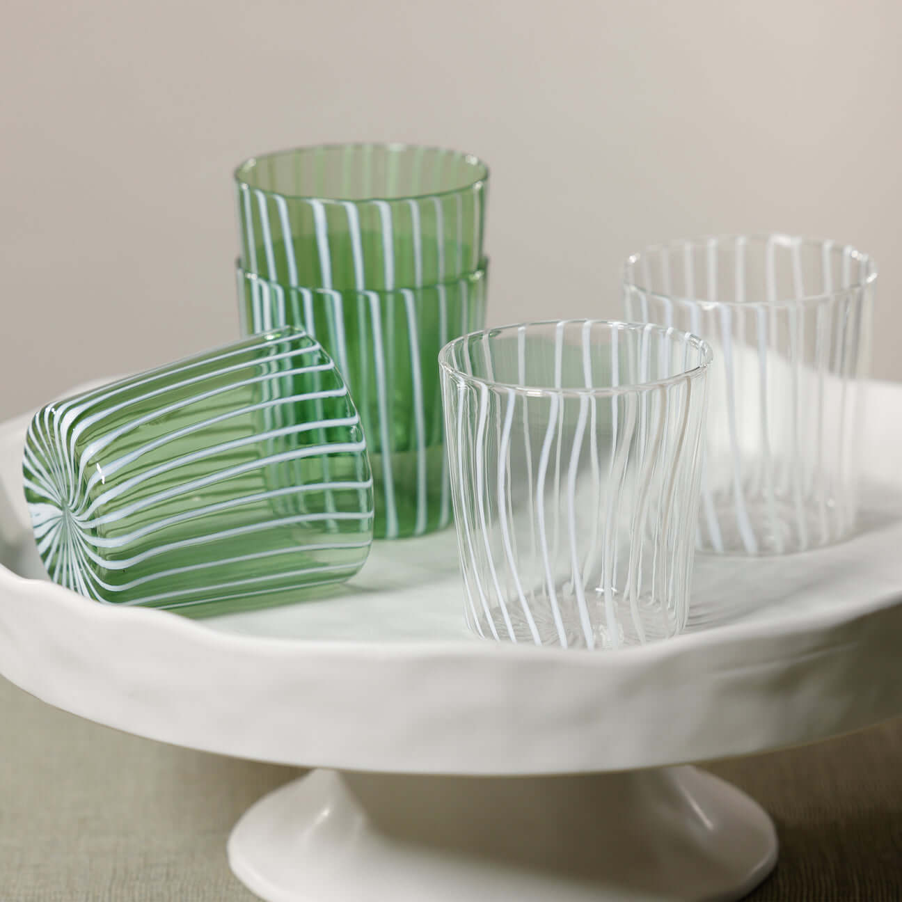 Marina White Stripe Glass Tumbler (Set of 6) displayed on a white serving tray with green and clear glasses.