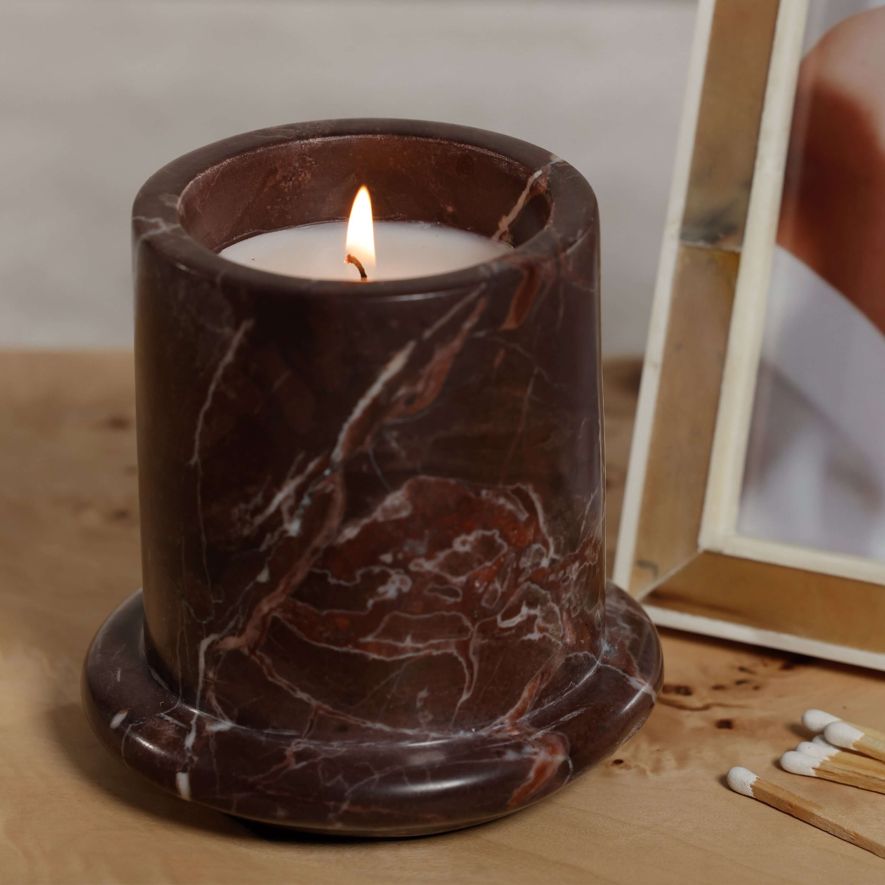 Marbella Scented Candle Jar with Cloche on a wooden surface, featuring a burning wick and natural marble design.