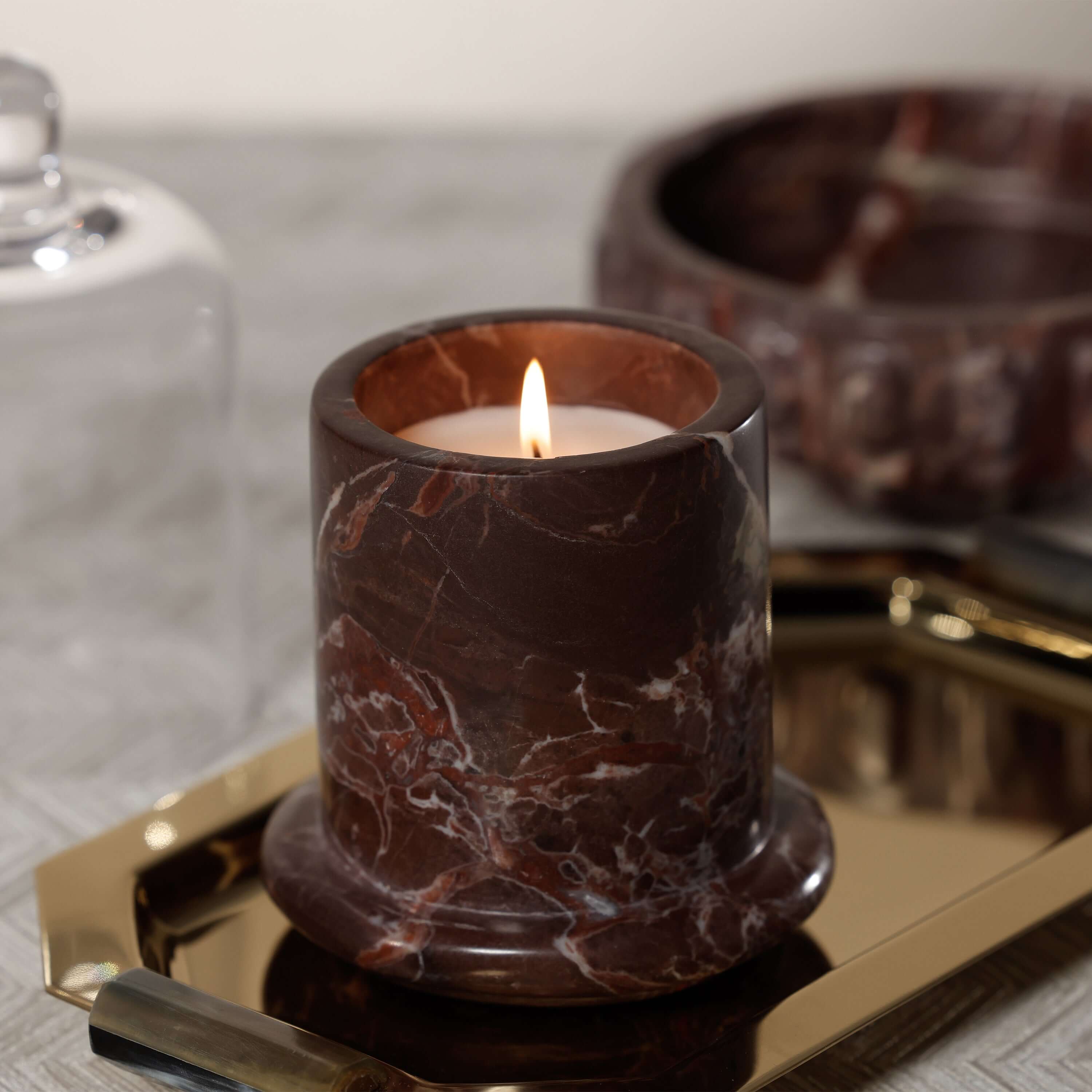 Marbella Scented Candle Jar with Cloche atop a gold tray, showcasing rich marble detail and warm flame.