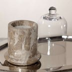 Marbella Scented Candle Jar with Cloche on a reflective tray, showcasing unique marble texture and glass cover.
