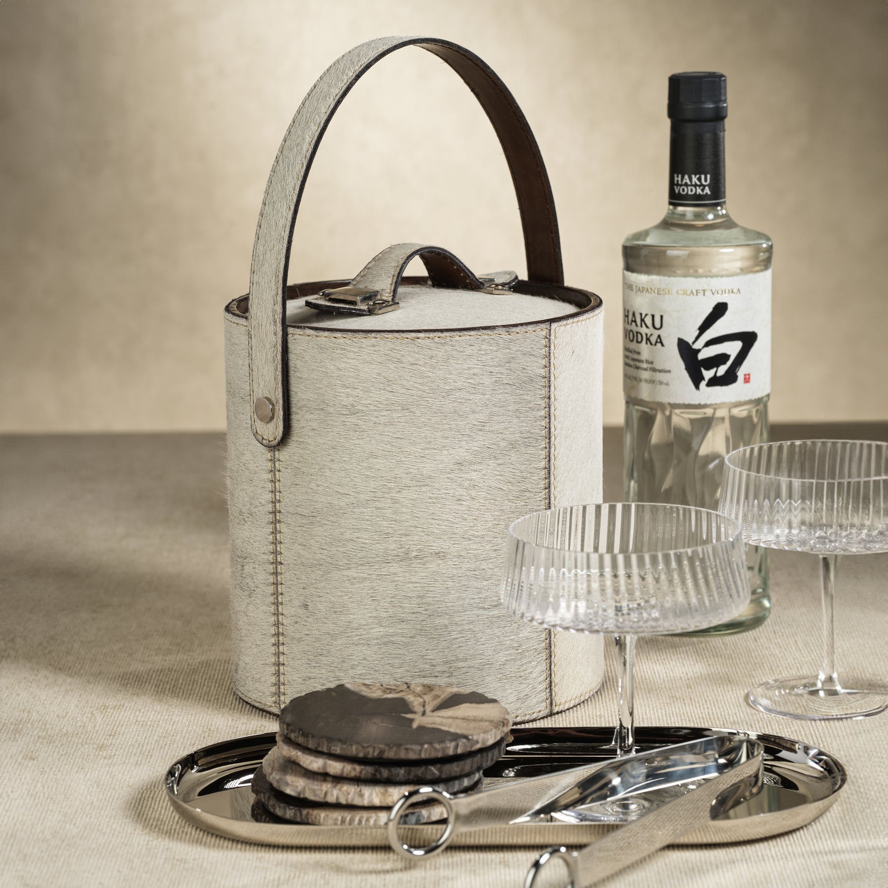 Bottle of Haku Vodka with an ice bucket, glasses, and coasters on a neutral background