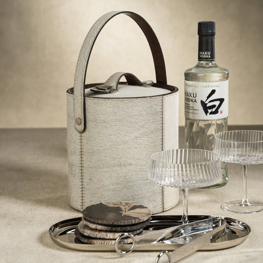 Bottle of Haku Vodka with an ice bucket, glasses, and coasters on a neutral background