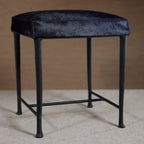 Black stool with a cushioned seat on a neutral background