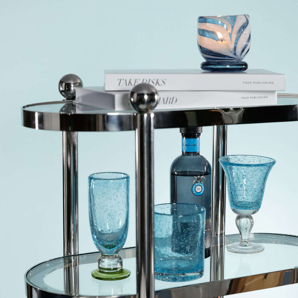 Three-Tier Étagère featuring blue glassware, candles, and books on a polished silver frame.