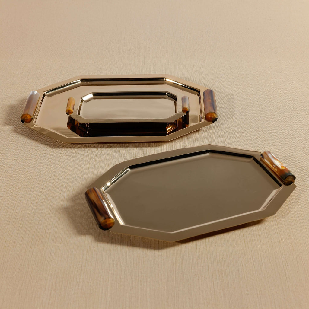 Two metallic trays with decorative handles on a beige surface