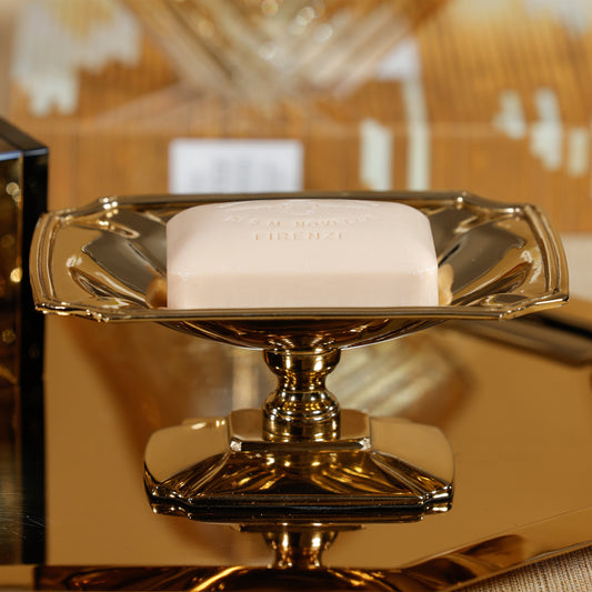 Gold soap dish with a bar of soap on a blurred background