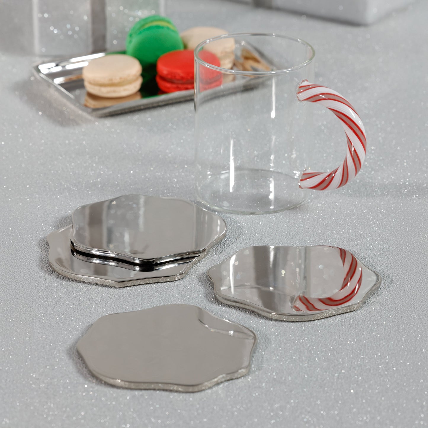 Clear mug with a candy cane handle on a reflective surface with silver coasters.